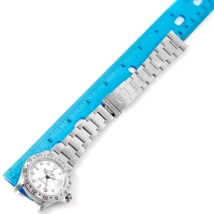 The image shows an angled view of a Rolex Explorer 16570 Men's Stainless Steel White Dial 16570 Men's Stainless Steel White Dial watch, highlighting its face, bezel, and bracelet band beside a ruler.