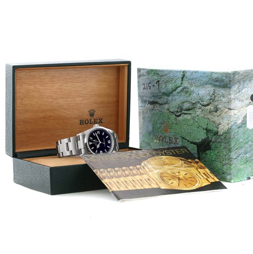 The Rolex Explorer 114270 Men's Stainless Steel Black Dial 114270 Men's Stainless Steel Black Dial watch is displayed inside its open box, along with an outer box and a brochure.