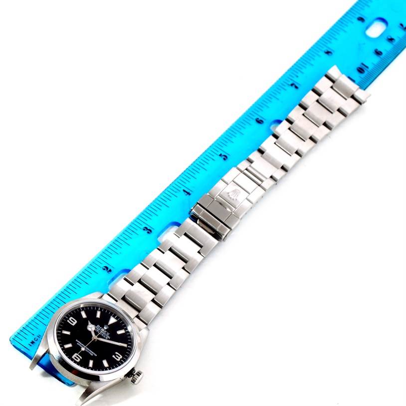 The image shows a Rolex Explorer 114270 Men's Stainless Steel Black Dial 114270 Men's Stainless Steel Black Dial watch laying flat with the band extended alongside a blue ruler.