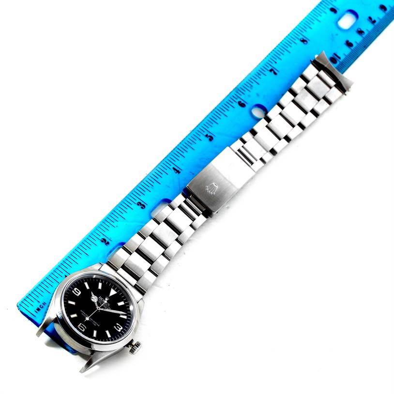 The image shows a Rolex Explorer 14270 Men's Stainless Steel Black Dial 14270 Men's Stainless Steel Black Dial watch with a stainless steel bracelet lying flat next to a blue ruler.