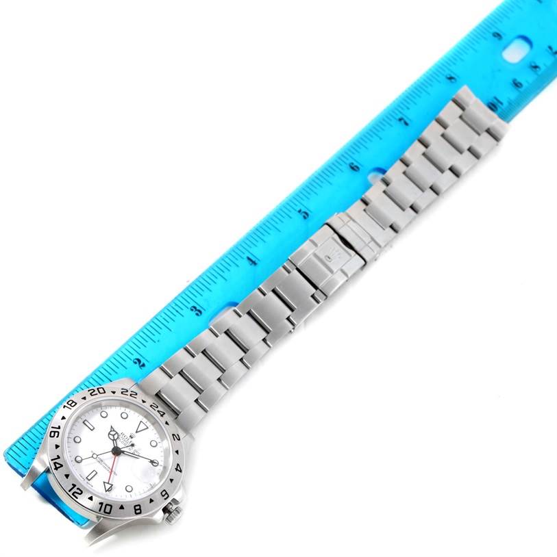 The Rolex Explorer 16570 Men's Stainless Steel White Dial 16570 Men's Stainless Steel White Dial watch is shown at a top-down angle with a blue ruler alongside it, displaying the full length of the watch and bracelet.