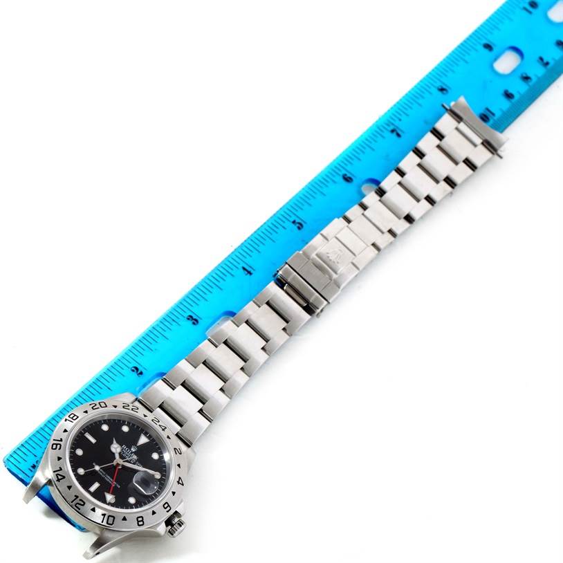 The image shows a Rolex Explorer 16570 Men
s Stainless Steel Black Dial 16570 Men
s Stainless Steel Black Dial watch, angled flatly, with its face and bracelet lying next to a blue ruler.