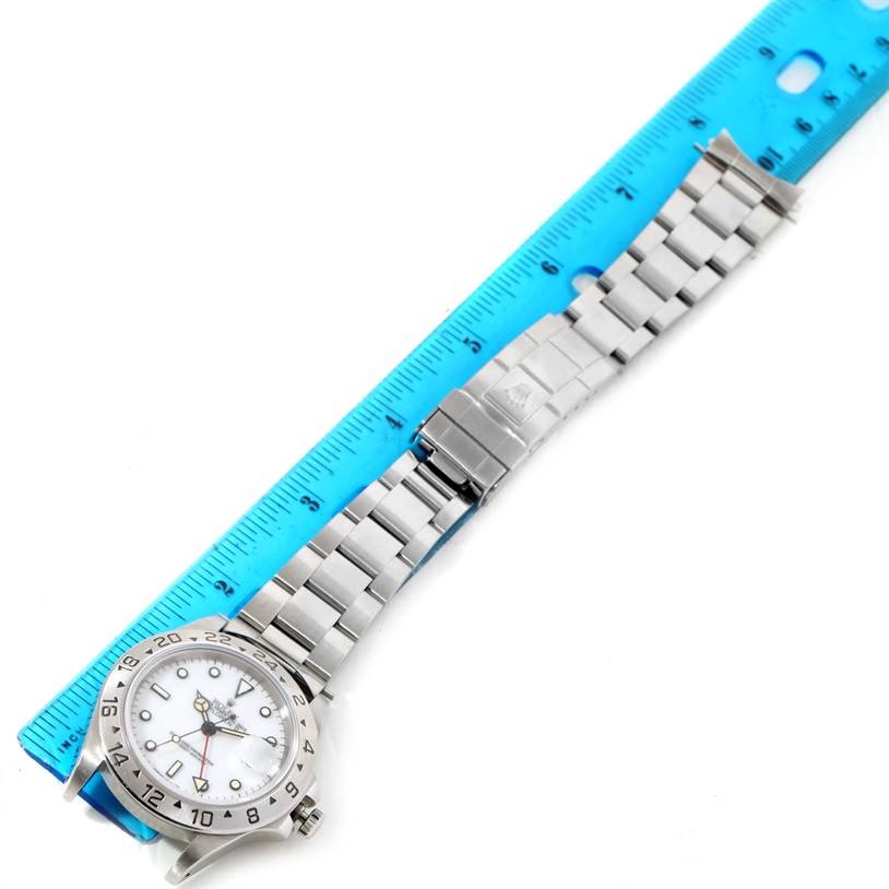 The Rolex Explorer 16570 Men's Stainless Steel White Dial 16570 Men's Stainless Steel White Dial watch is shown laid out flat, featuring its face, bezel, and bracelet next to a blue ruler.