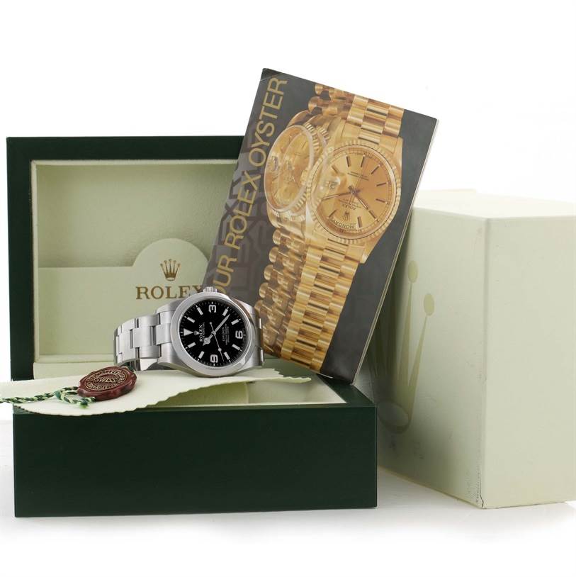 The image shows a Rolex Explorer 214270 Men's Stainless Steel Black Dial 214270 Men's Stainless Steel Black Dial watch in an open box with its manual, hang tag, and seal, viewed from a front angle.