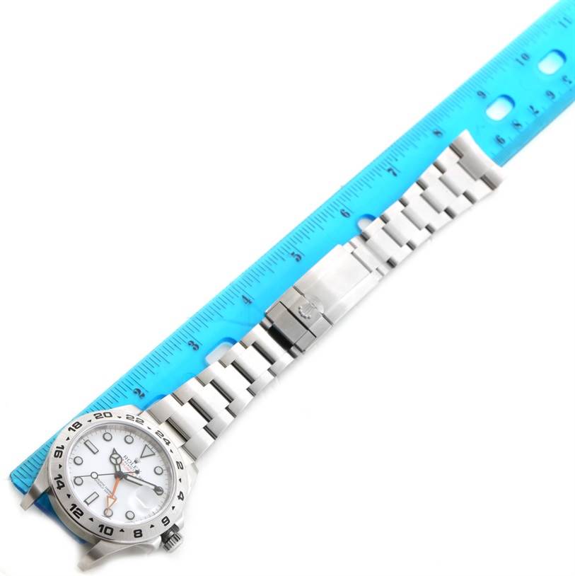 This image displays a Rolex Explorer 216570WSO Men's Stainless Steel White Dial 216570WSO Men's Stainless Steel White Dial watch laying flat with its stainless steel bracelet extended alongside a blue ruler.