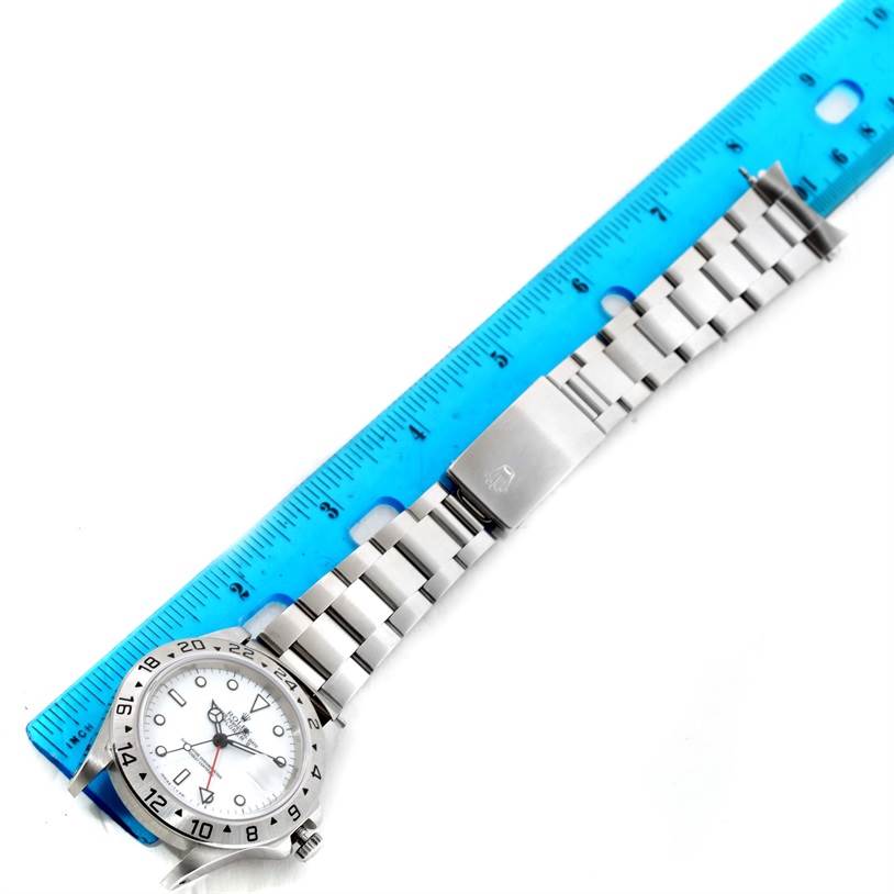 The Rolex Explorer 16570 Men's Stainless Steel White Dial 16570 Men's Stainless Steel White Dial watch is shown laid flat next to a blue ruler, highlighting its metal bracelet and clasp.