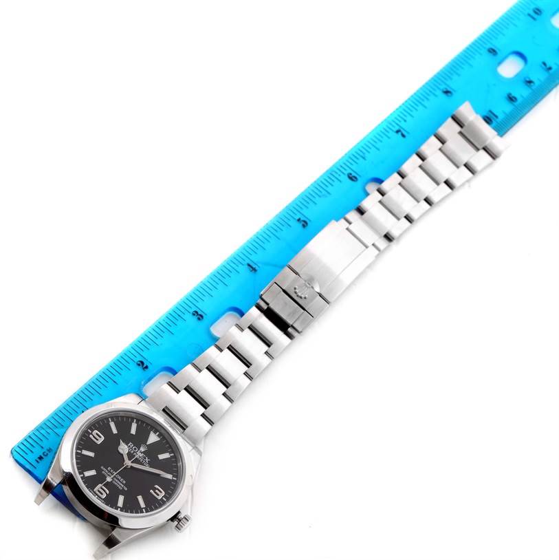 The image shows a Rolex Explorer 214270 Men's Stainless Steel Black Dial 214270 Men's Stainless Steel Black Dial watch laid flat with its band extended alongside a blue ruler for measurement.