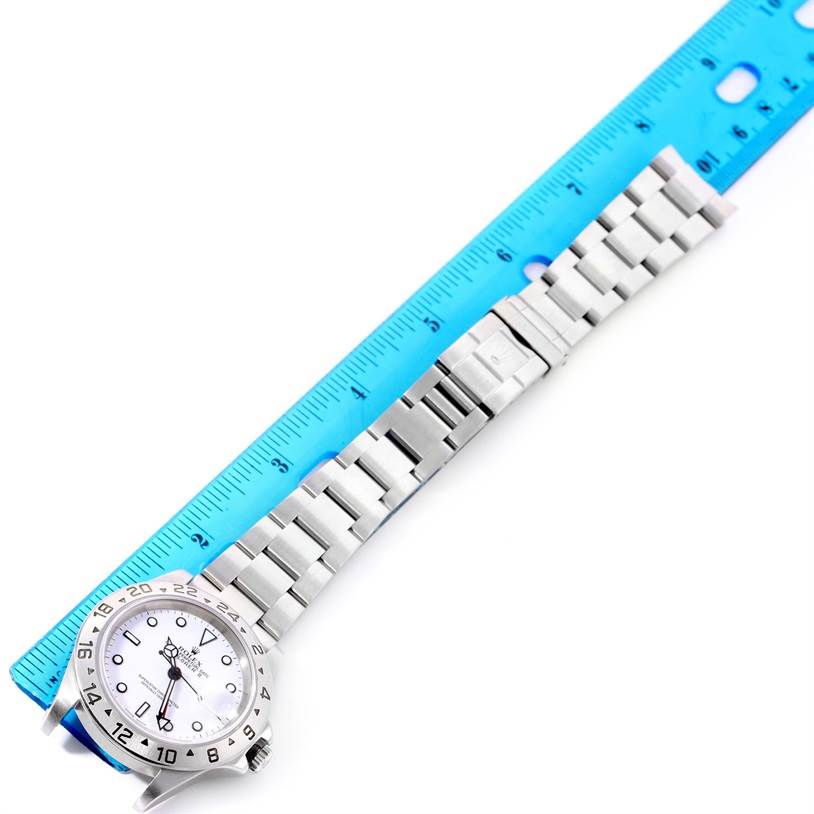 The image shows a Rolex Explorer 16570 Men's Stainless Steel White Dial 16570 Men's Stainless Steel White Dial watch with a blue ruler measuring its silver metal bracelet, viewed from above.
