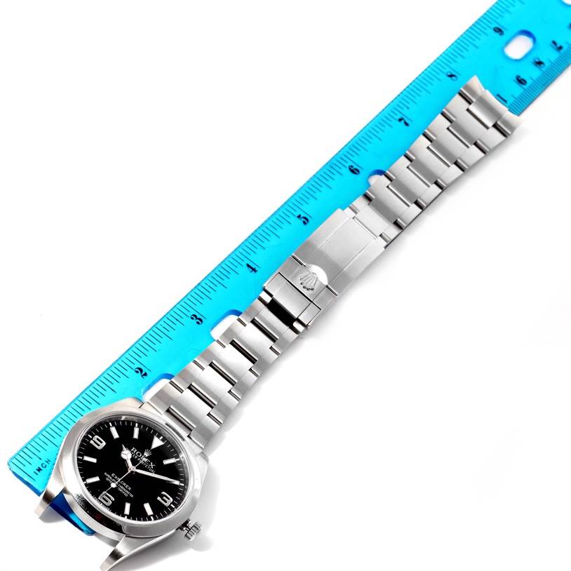 The image shows a horizontal view of a Rolex Explorer 214270 Men's Stainless Steel Black Dial 214270 Men's Stainless Steel Black Dial watch, displaying the watch face and the full metal band next to a blue ruler for scale.