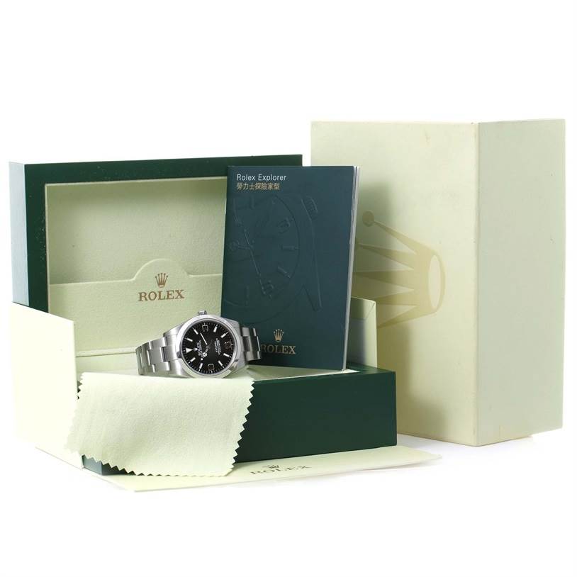The image shows a Rolex Explorer 214270 Men's Stainless Steel Black Dial 214270 Men's Stainless Steel Black Dial watch positioned in its open box with a booklet and cleaning cloth included.