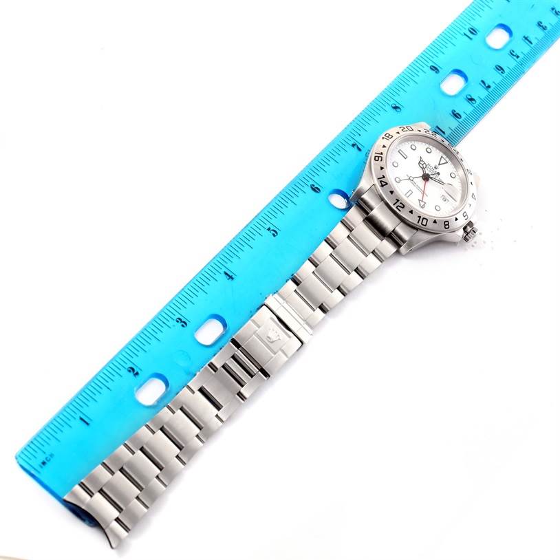 The image shows a top-down view of a Rolex Explorer 16570 Men's Stainless Steel White Dial 16570 Men's Stainless Steel White Dial watch, including its face, bezel, and metal bracelet, alongside a blue ruler.