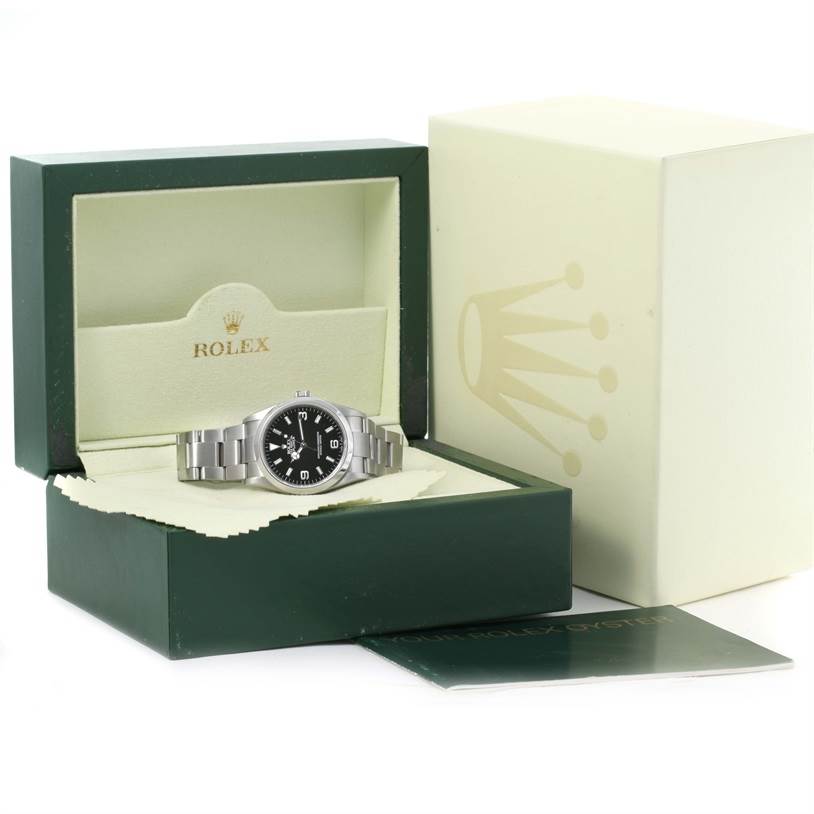 The Rolex Explorer 114270 Men's Stainless Steel Black Dial 114270 Men's Stainless Steel Black Dial watch is shown placed in an open green and cream-colored Rolex box, accompanied by booklets and additional packaging.