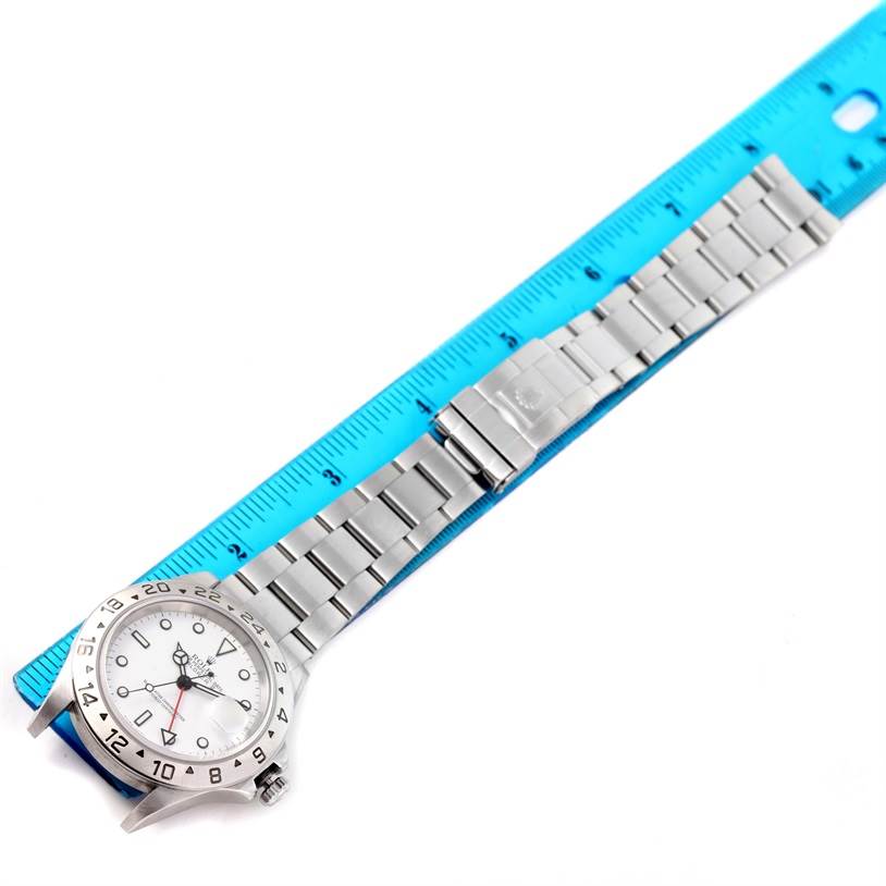 The image shows a Rolex Explorer 16570 Men's Stainless Steel White Dial 16570 Men's Stainless Steel White Dial model watch laid flat with a blue ruler beside it, displaying the dial, bezel, and bracelet.