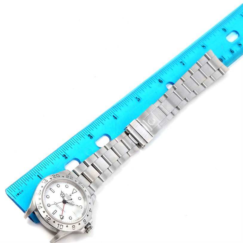 This image shows a side angle of the Rolex Explorer 16570 Men's Stainless Steel White Dial 16570 Men's Stainless Steel White Dial watch, highlighting its face, bezel, and bracelet laid next to a ruler.