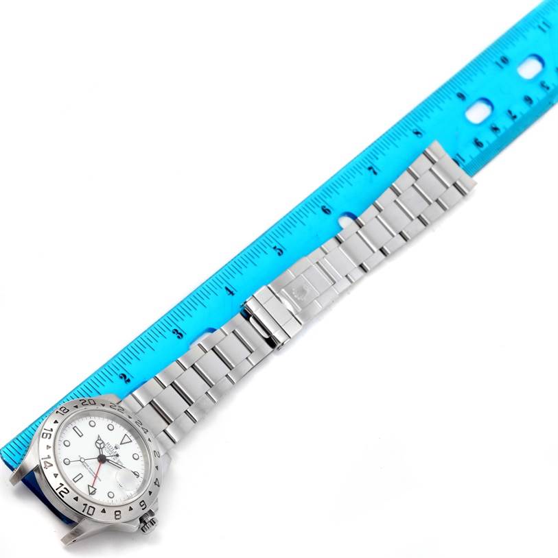 This image shows a Rolex Explorer 16570 Men's Stainless Steel White Dial 16570 Men's Stainless Steel White Dial watch with a silver metal bracelet next to a blue ruler for measurement.