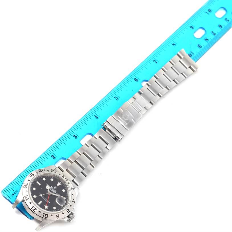 The Rolex Explorer 16570 Men's Stainless Steel Black Dial 16570 Men's Stainless Steel Black Dial model watch is shown laying flat with the face, bezel, bracelet, and clasp visible next to a blue ruler.