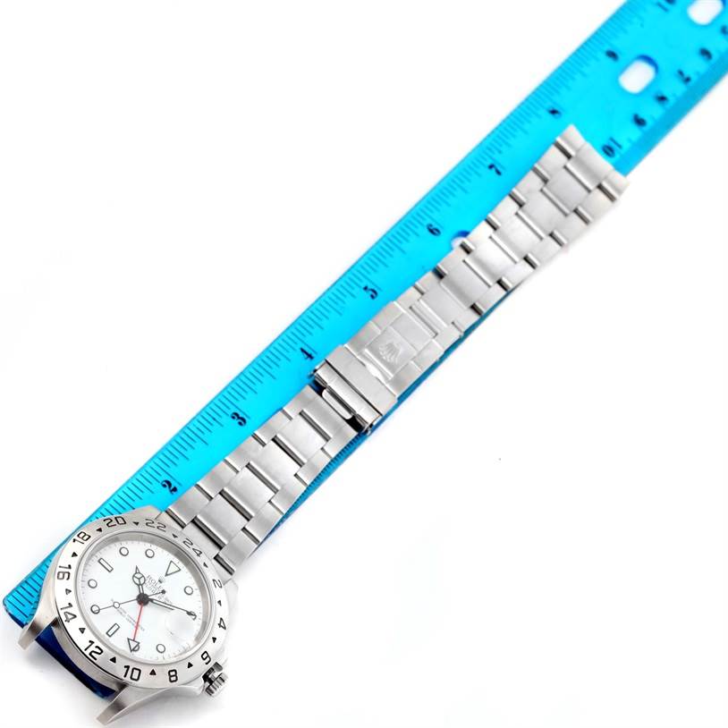 The Rolex Explorer 16570 Men's Stainless Steel White Dial 16570 Men's Stainless Steel White Dial watch is shown with a top-down view, displaying its face, bezel, and metal bracelet next to a blue ruler.