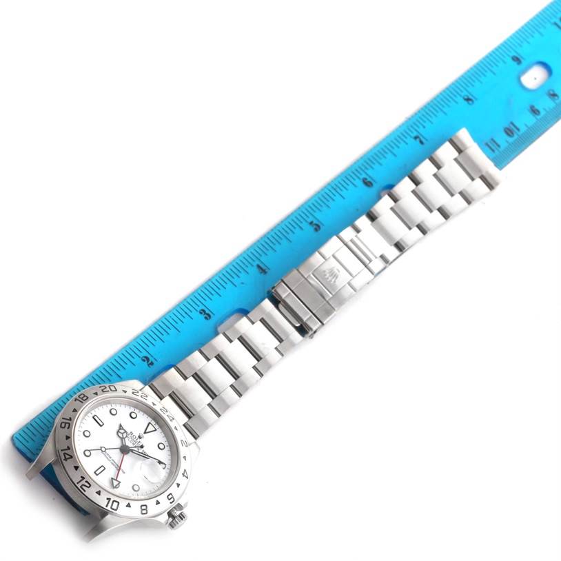 The Rolex Explorer 16570 Men's Stainless Steel White Dial 16570 Men's Stainless Steel White Dial watch is shown from a top-down angle alongside a blue ruler, highlighting its bracelet and clasp.