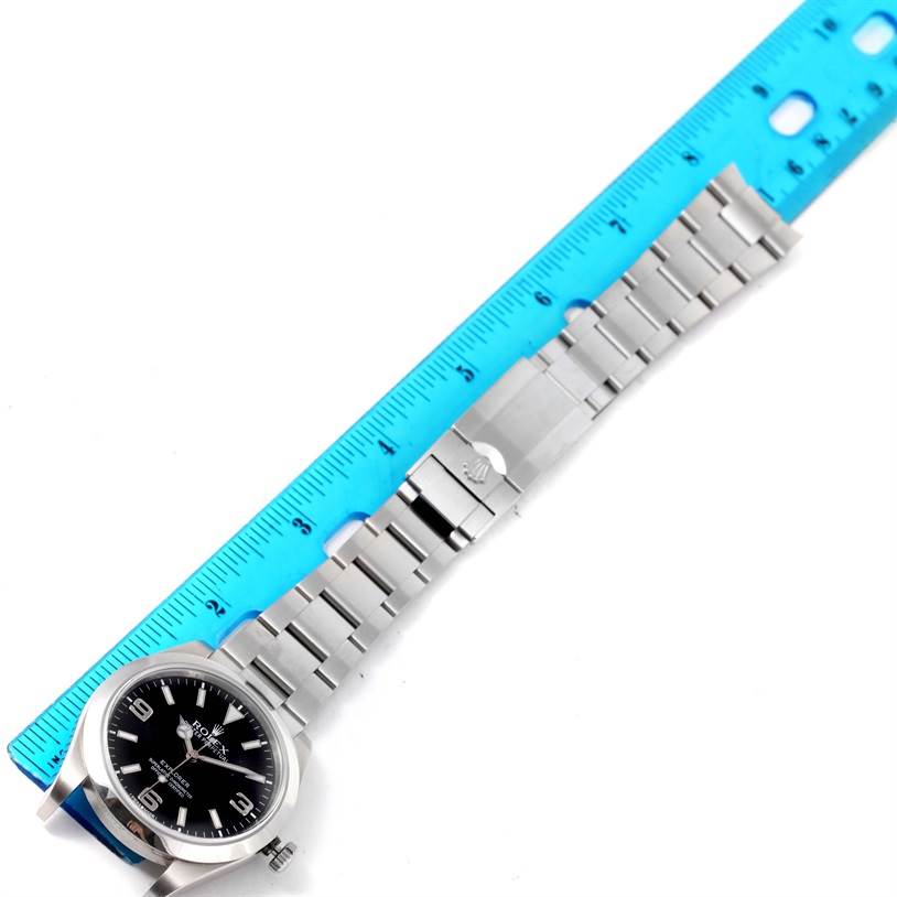 The image shows a Rolex Explorer 214270 Men's Stainless Steel Black Dial 214270 Men's Stainless Steel Black Dial watch laid flat with a blue ruler measuring its length, displaying the face, bracelet, and clasp.