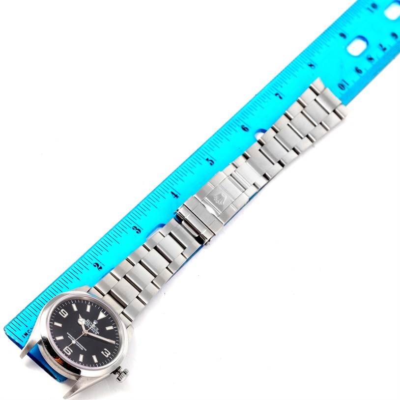 The Rolex Explorer 114270 Men's Stainless Steel Black Dial 114270 Men's Stainless Steel Black Dial watch is shown from a top-down angle, displaying its face, bracelet, and clasp beside a ruler.