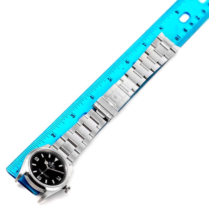 The image shows the Rolex Explorer 114270 Men's Stainless Steel Black Dial 114270 Men's Stainless Steel Black Dial watch from a top-down angle, displaying its face, band, and a part of a blue ruler.