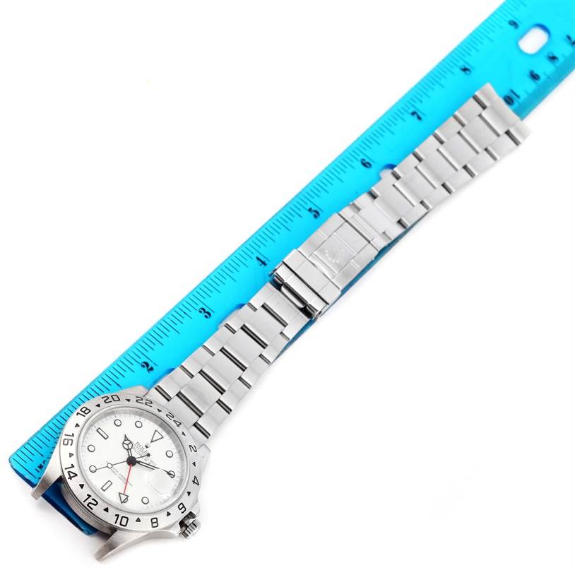 The Rolex Explorer 16570 Men's Stainless Steel White Dial 16570 Men's Stainless Steel White Dial model watch is photographed from an overhead angle showing its face, bezel, and extended bracelet next to a blue ruler.