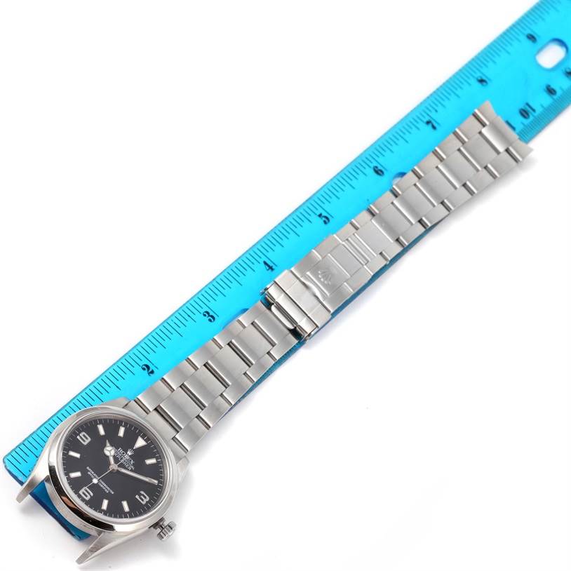 The image shows a Rolex Explorer 114270 Men
s Stainless Steel Black Dial 114270 Men
s Stainless Steel Black Dial watch laid flat next to a ruler, displaying the watch face, bracelet, and clasp.