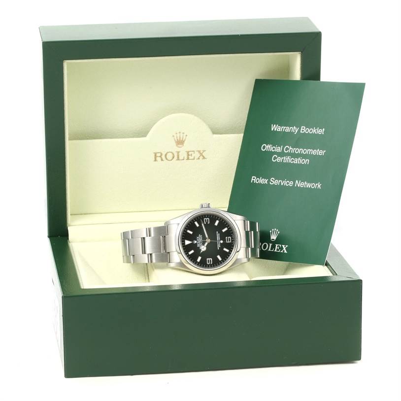 The Explorer model Rolex watch is shown at an angle inside an open green box, alongside warranty and certification booklets.