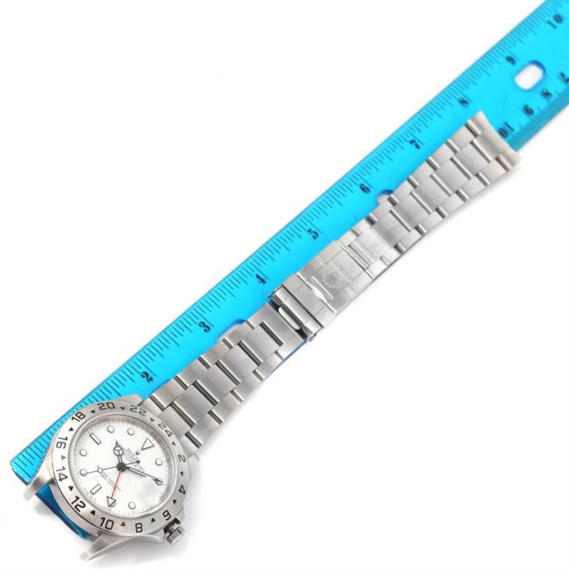 The Rolex Explorer 16570 Men's Stainless Steel White Dial 16570 Men's Stainless Steel White Dial watch is shown laying flat with the face, bezel, bracelet, and clasp visible next to a blue ruler for scale.