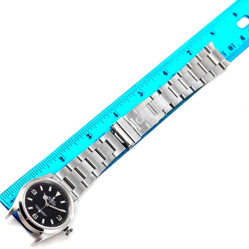 The image shows a full view of a Rolex Explorer 114270 Men's Stainless Steel Black Dial 114270 Men's Stainless Steel Black Dial model watch laid next to a blue ruler.