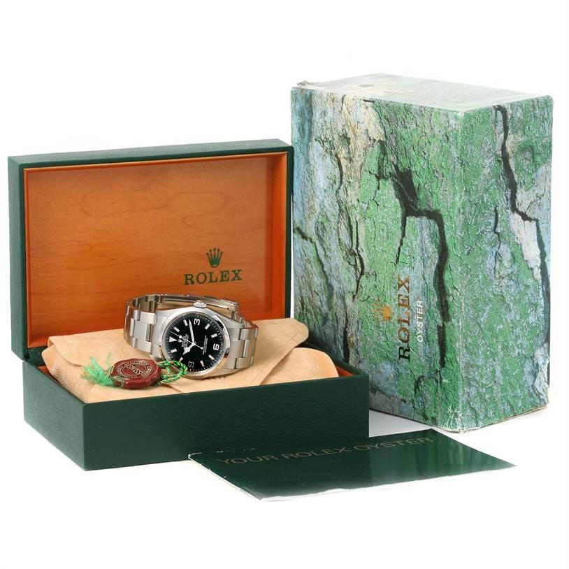 This image shows a Rolex Explorer 114270 Men's Stainless Steel Black Dial 114270 Men's Stainless Steel Black Dial watch placed inside an open green and wooden Rolex box, with its outer packaging and paperwork beside it.