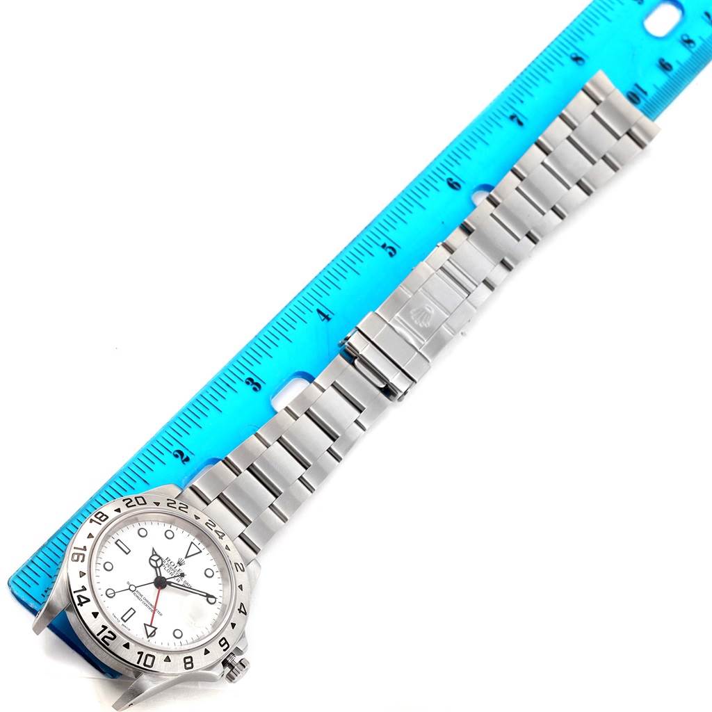 The image shows a Rolex Explorer 16570 Men
s Stainless Steel White Dial 16570 Men
s Stainless Steel White Dial watch laid flat, next to a blue ruler, displaying its bezel, dial, and bracelet.