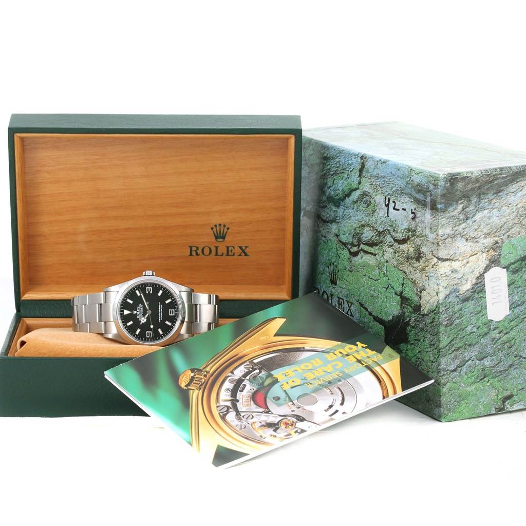 The image shows a Rolex Explorer 114270 Men's Stainless Steel Black Dial 114270 Men's Stainless Steel Black Dial watch inside an open box, along with a booklet and outer packaging.