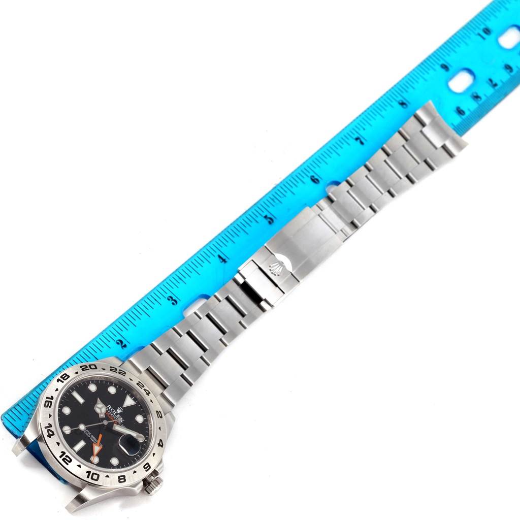 The Rolex Explorer 216570 Men
s Black Dial 216570 Men
s Black Dial watch is shown flat with its full metal bracelet and clasp, alongside a blue measuring ruler.