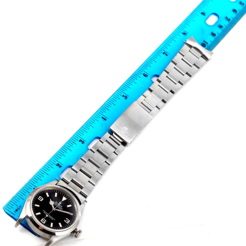 The image shows a top view of a Rolex Explorer 14270 Men
s Stainless Steel Black Dial 14270 Men
s Stainless Steel Black Dial watch, highlighting its face and stainless steel bracelet alongside a ruler for scale.