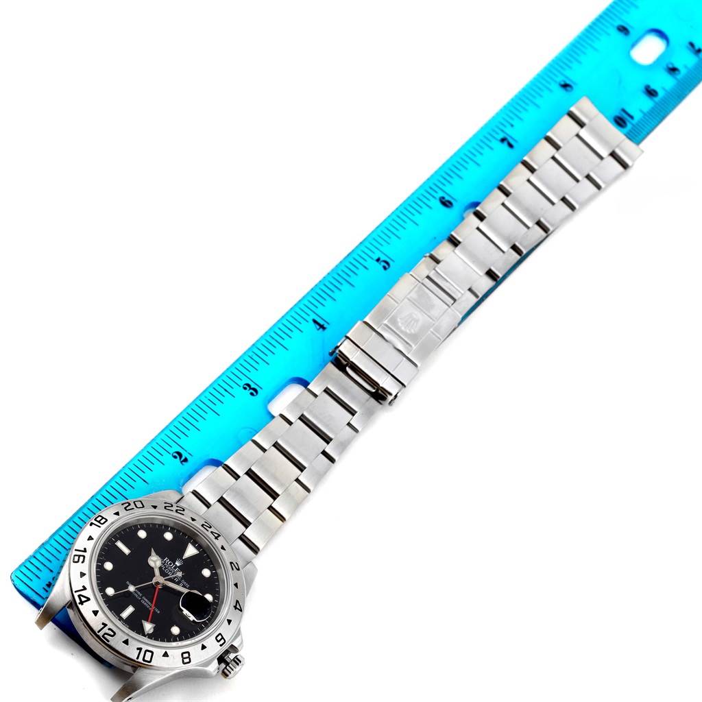 The Rolex Explorer 16570 Men's Stainless Steel Black Dial 16570 Men's Stainless Steel Black Dial watch is shown from a top-down angle, accompanying a blue ruler for scale.