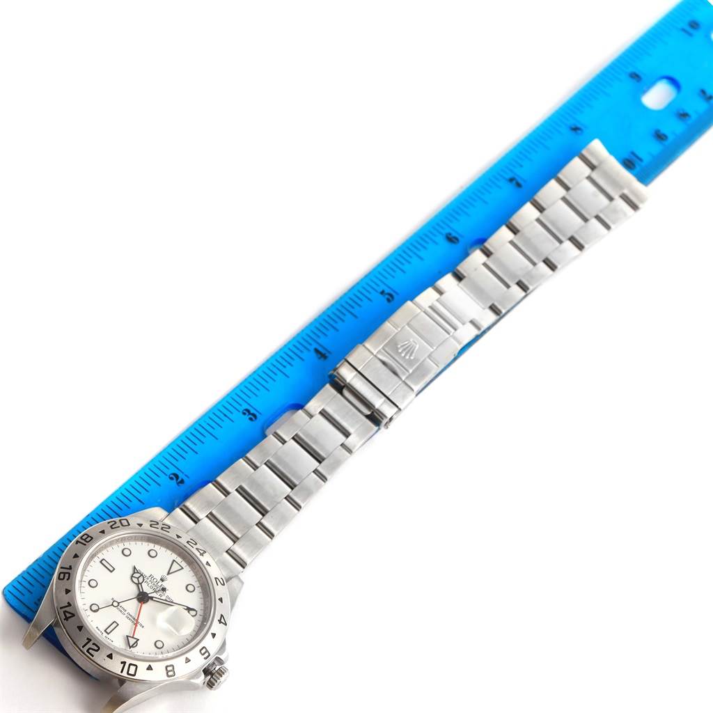 This image shows a top view of a Rolex Explorer 16570 Men's Stainless Steel White Dial 16570 Men's Stainless Steel White Dial watch laid next to a blue ruler.