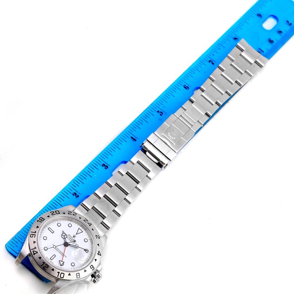 The Rolex Explorer 16570 Men's Stainless Steel White Dial 16570 Men's Stainless Steel White Dial watch is shown from a top-down angle, highlighting its face and full metal band alongside a blue ruler for scale.