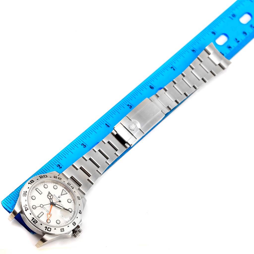 The Rolex Explorer 216570 Men
s Stainless Steel White Dial 216570 Men
s Stainless Steel White Dial watch is shown flat with its face visible, next to a blue ruler for measurement.