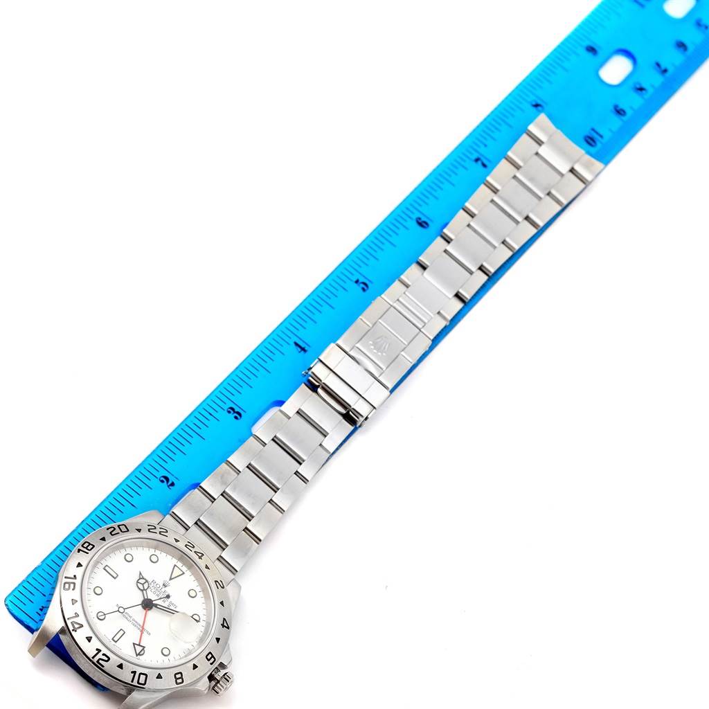 The image shows a Rolex Explorer 16570 Men
s Stainless Steel White Dial 16570 Men
s Stainless Steel White Dial watch band with a clasp and part of the watch face, measured against a blue ruler.