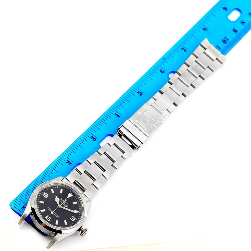 The image shows a Rolex Explorer 114270 Men's Stainless Steel Black Dial 114270 Men's Stainless Steel Black Dial watch laid next to a blue ruler, displaying the watch face, crown, and full bracelet.