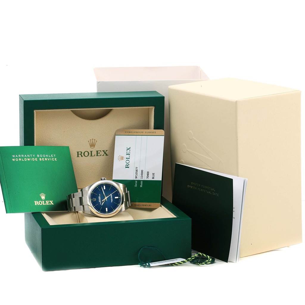 The image shows a Rolex Explorer 114300 Men's Stainless Steel Blue Dial 114300 Men's Stainless Steel Blue Dial watch with box, warranty booklet, and tags, photographed from the front angle.