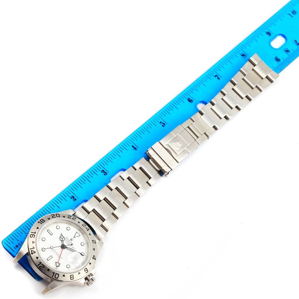 The image shows a Rolex Explorer 16570 Men's Stainless Steel White Dial 16570 Men's Stainless Steel White Dial watch placed alongside a blue ruler, displaying its stainless steel strap and clasp.