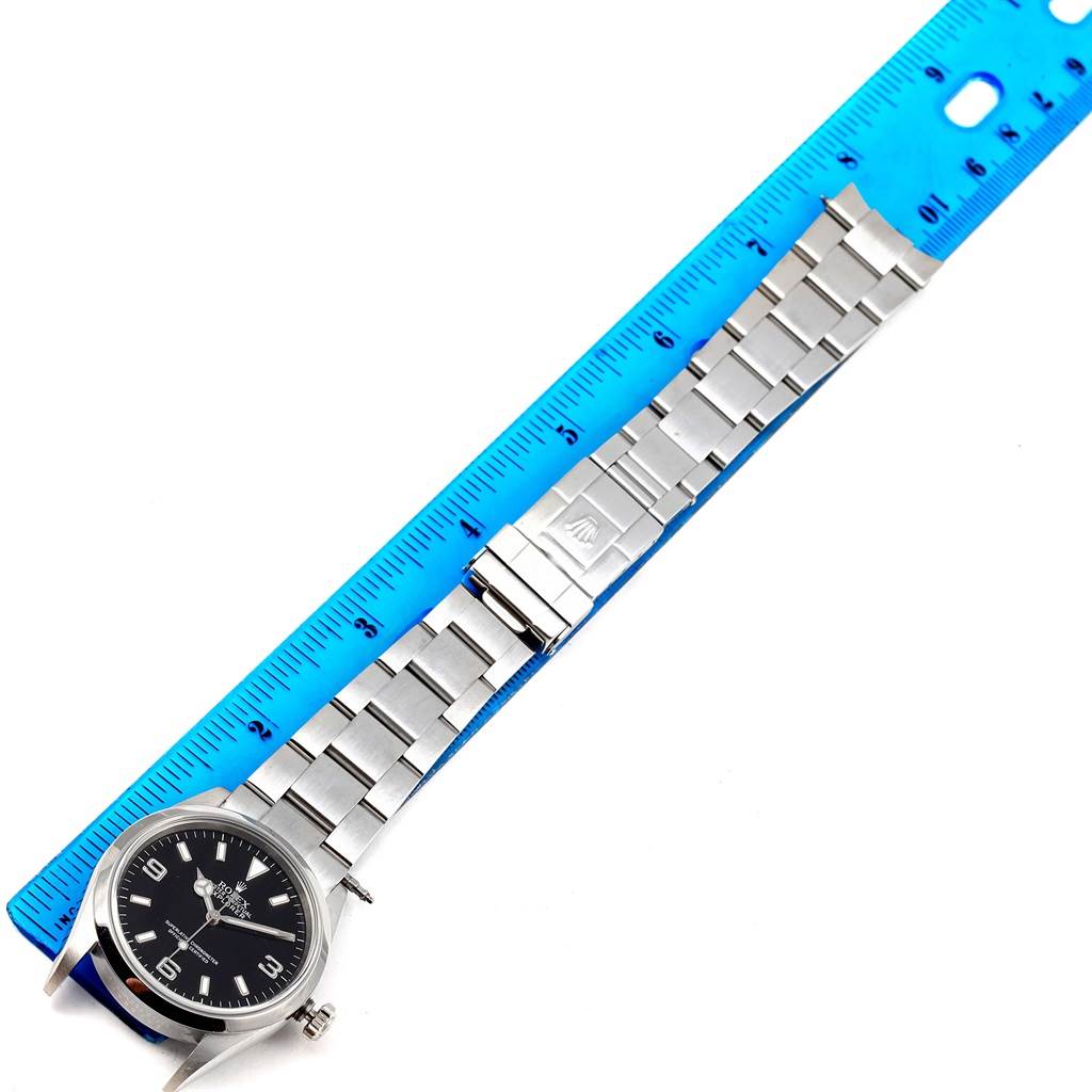 The image shows a Rolex Explorer 114270 Men's Stainless Steel Black Dial 114270 Men's Stainless Steel Black Dial watch laying flat with a blue ruler aligned next to its stainless steel bracelet.