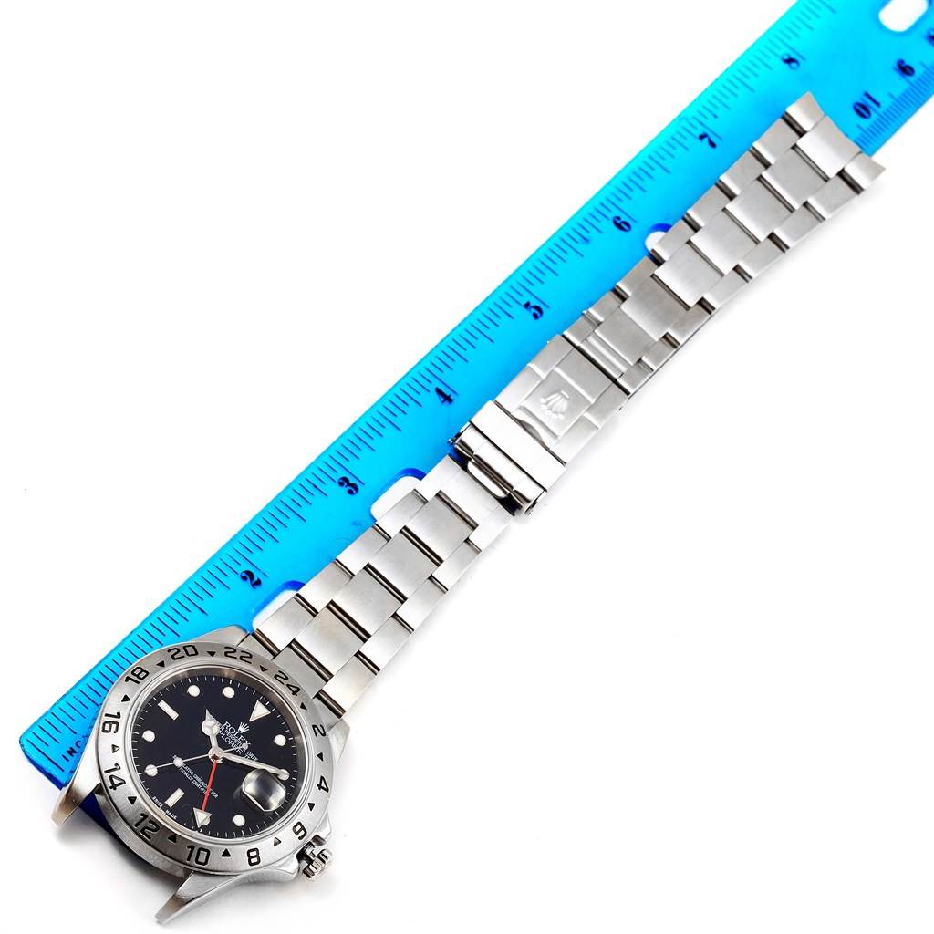 The Rolex Explorer 16570 Men's Stainless Steel Black Dial 16570 Men's Stainless Steel Black Dial watch is shown from an overhead angle, displaying its face, bezel, and metal strap next to a blue ruler.