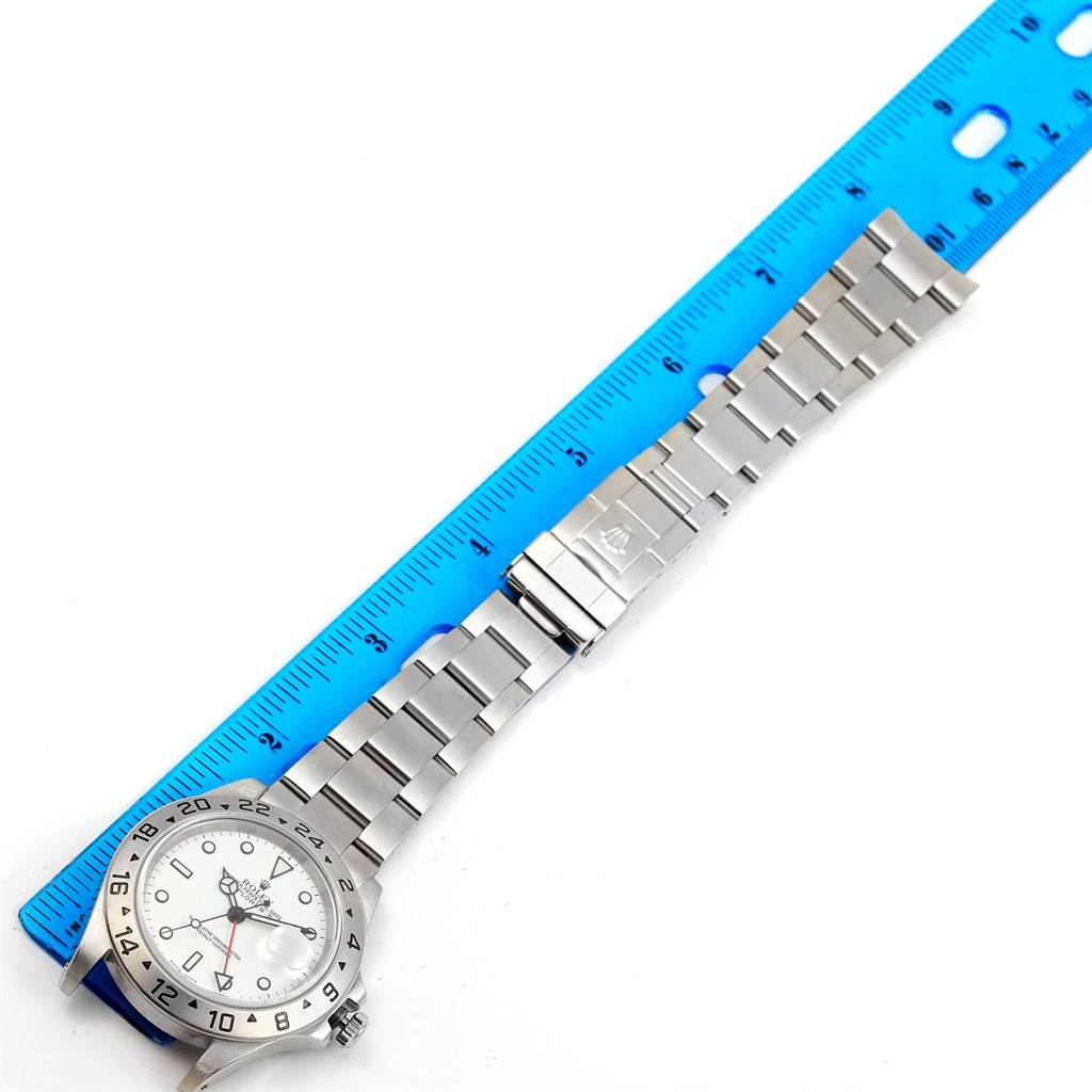 The image shows a Rolex Explorer 16570 Men's Stainless Steel White Dial 16570 Men's Stainless Steel White Dial watch with a close-up angle of its face, bracelet, and clasp next to a ruler.