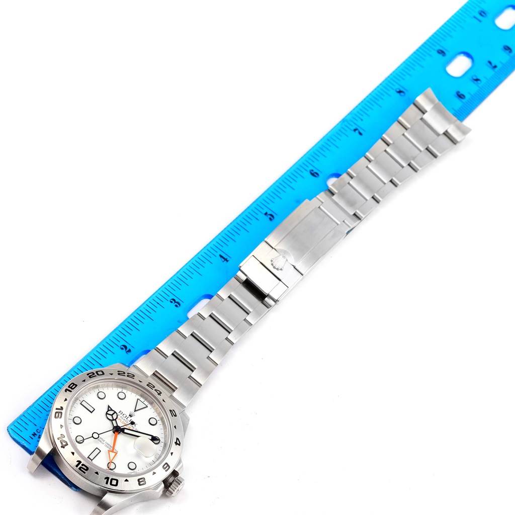 The Rolex Explorer 216570 Men's Stainless Steel White Dial 216570 Men's Stainless Steel White Dial watch is shown from above, displaying the face, bezel, crown, and full metal bracelet beside a blue ruler for scale.