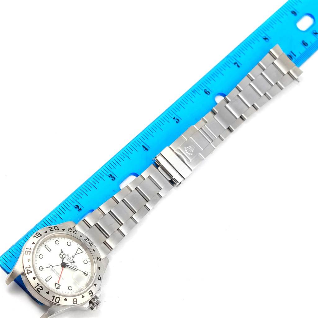The image shows a Rolex Explorer 16570 Men's Stainless Steel White Dial 16570 Men's Stainless Steel White Dial watch placed next to a blue ruler, displaying its bracelet and clasp.