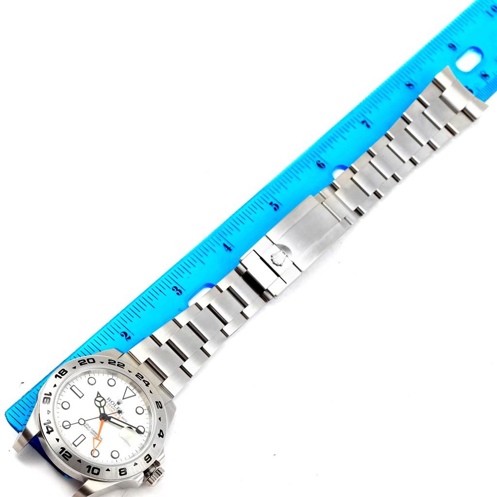This image shows a Rolex Explorer 216570 Men's Stainless Steel White Dial 216570 Men's Stainless Steel White Dial model watch laid flat with its bracelet extended next to a ruler.