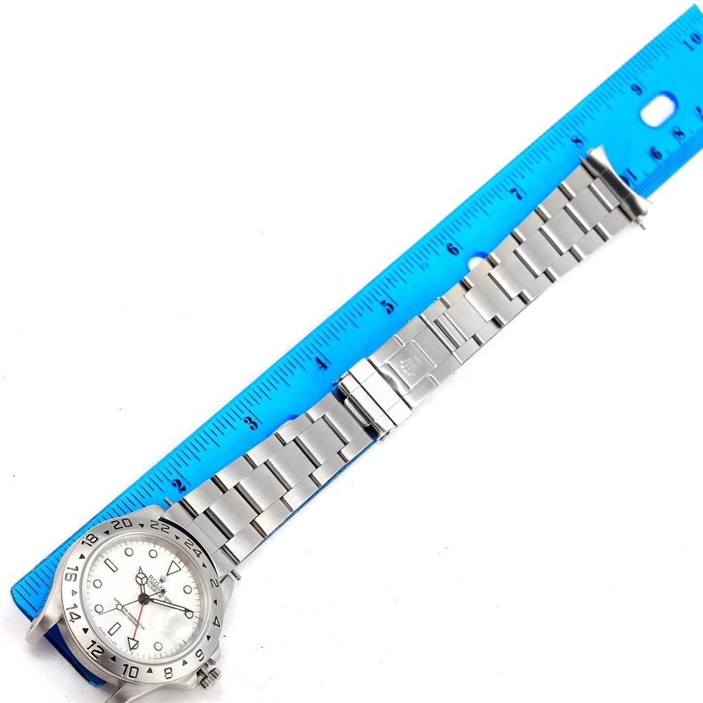 The Rolex Explorer 16570 Men's Stainless Steel White Dial 16570 Men's Stainless Steel White Dial watch is shown from the top view, highlighting the face, bezel, and full bracelet laid beside a blue ruler.